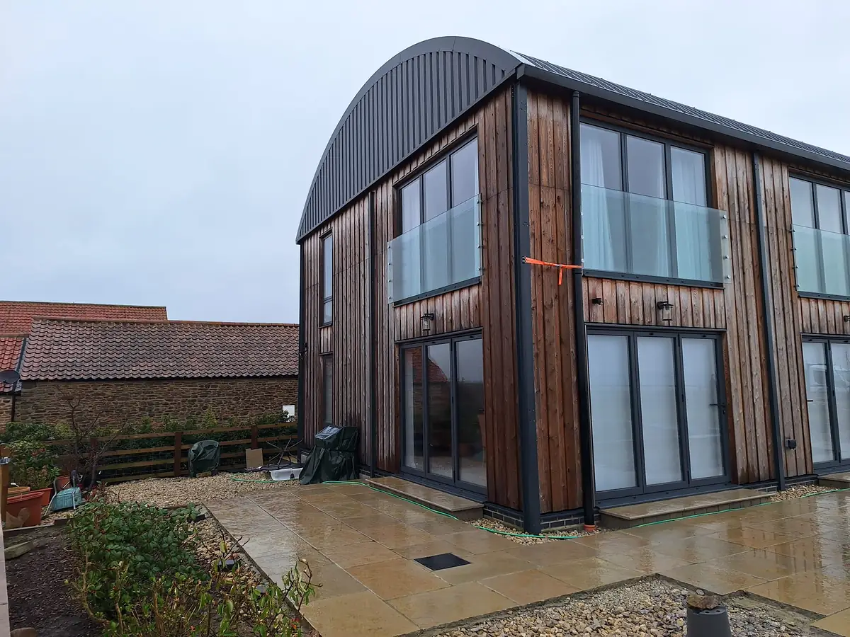 Timber clad new build at Whenby with a curved metal roof and glazed gable